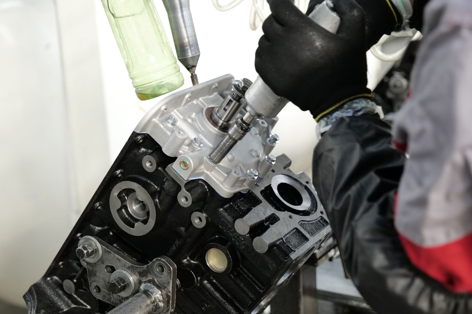 Real photograph of gloved hands assembling an engine component with a precision tool