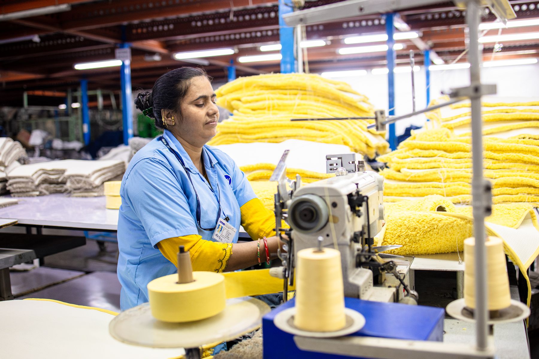 Real photograph of a worker sewing yellow fabric on an industrial machine in India