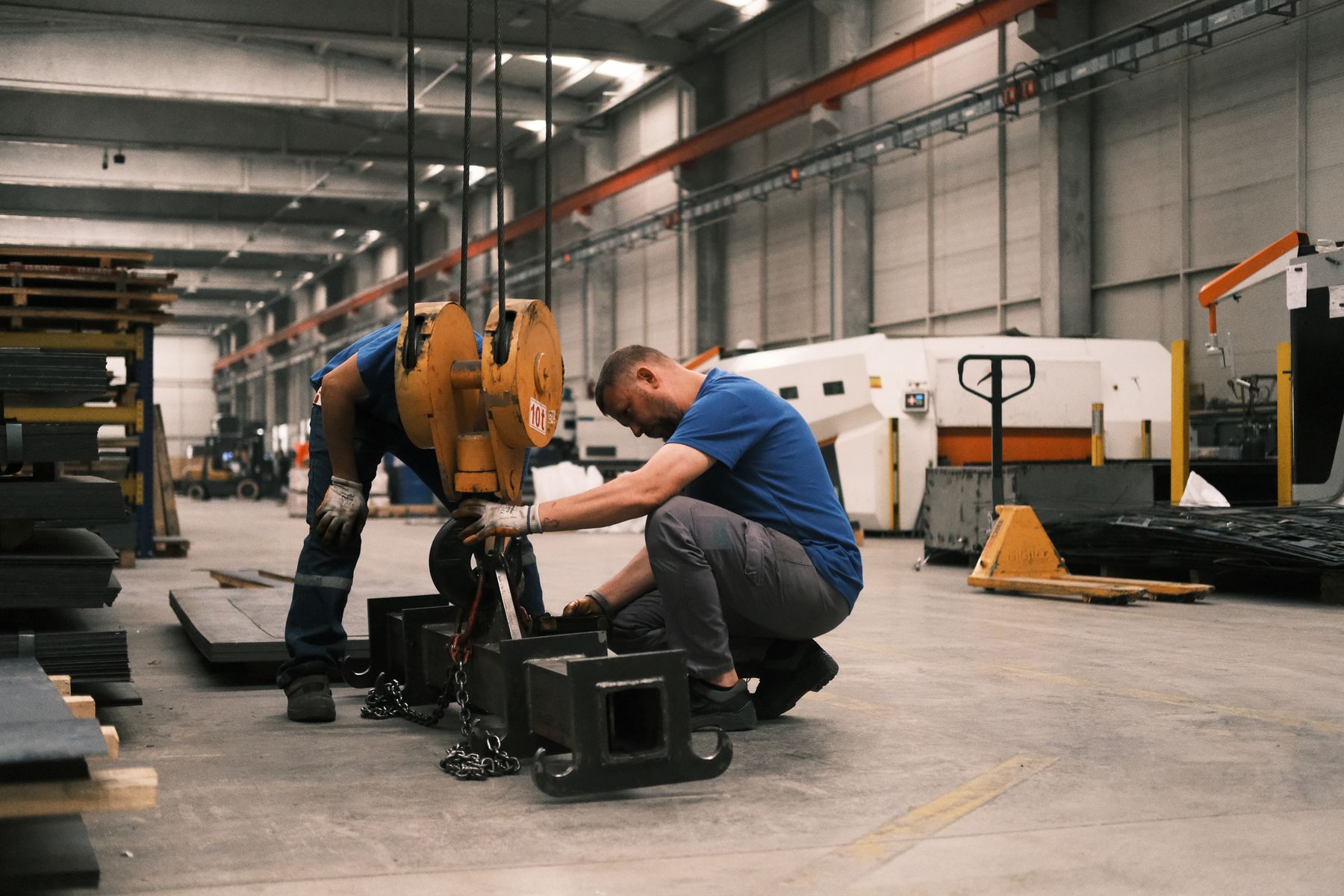 Real photograph of two workers positioning a crane hook and metal component in a factory in Konya, Turkey